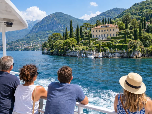 Fahrgäste auf dem Deck einer Fähre am Comer See betrachten eine Villa am Ufer